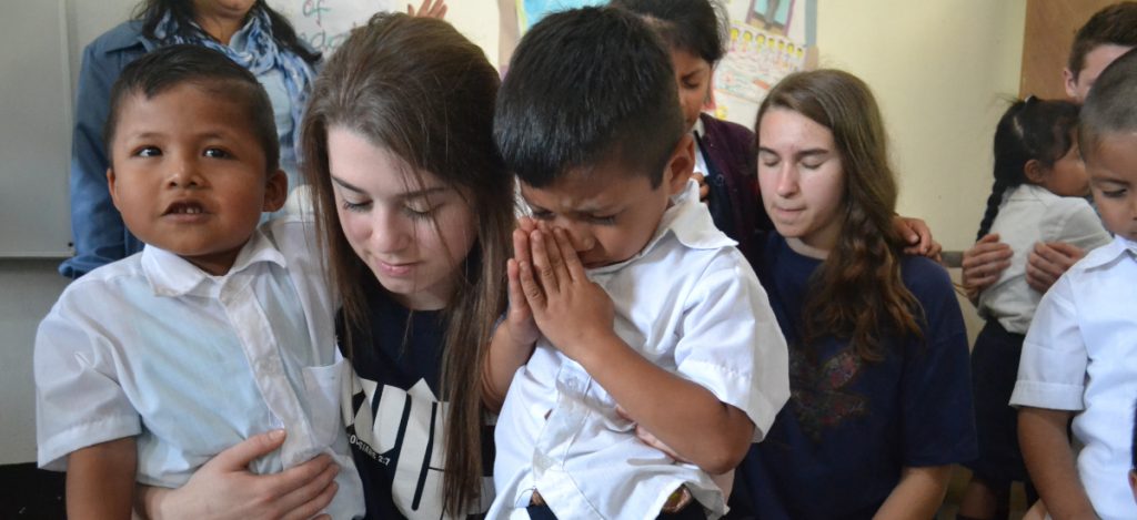 young adult praying with two vida students