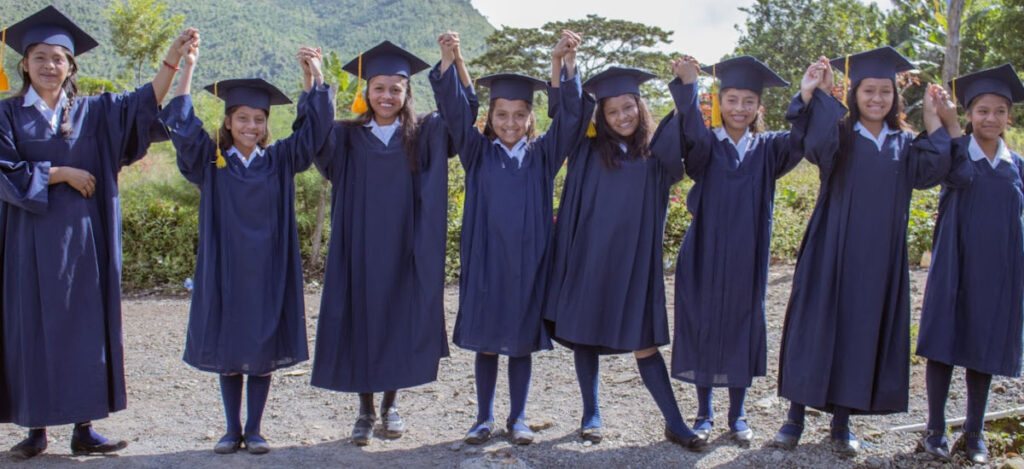 Guatemalan teens in black grad caps and gowns standing in a row with joined hands raised