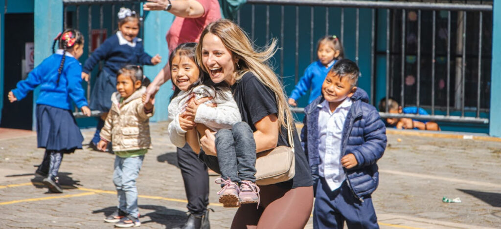 A young Guatemalan girl with a big smile in the arms of a North American woman with an equally big smile running in the midst of a group of kids playing some sort of game